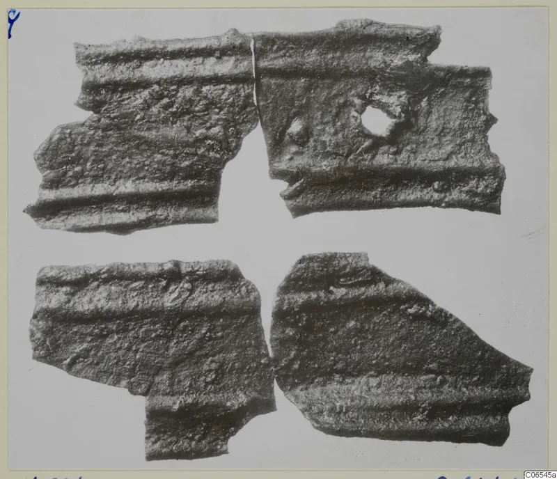 Four fragments of corroded bronze mountings with parallel raised ridges, one with a round hole, on a pale background