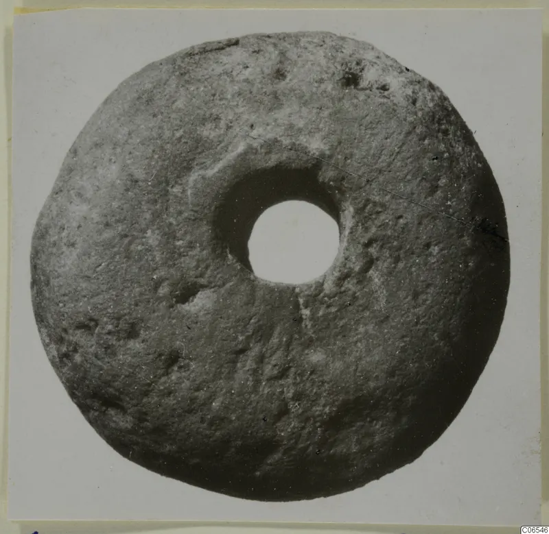 Disc-shaped object with a large central hole, grey-brown with a rough, pitted surface, from Vouni