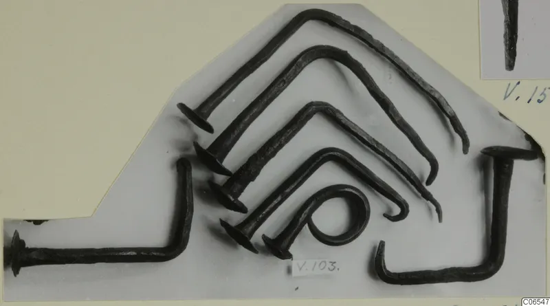 Several dark, corroded metal nails with flat heads and bent shanks, laid out on a grey card with a number label V.103.