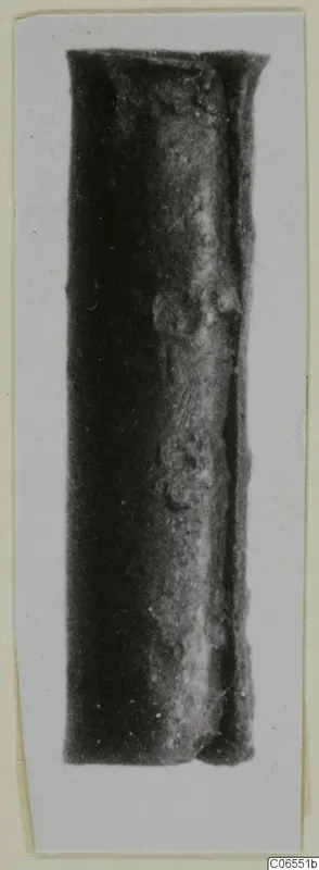 Bronze fragment, a dark cylindrical metal piece with a flared top rim, photographed upright