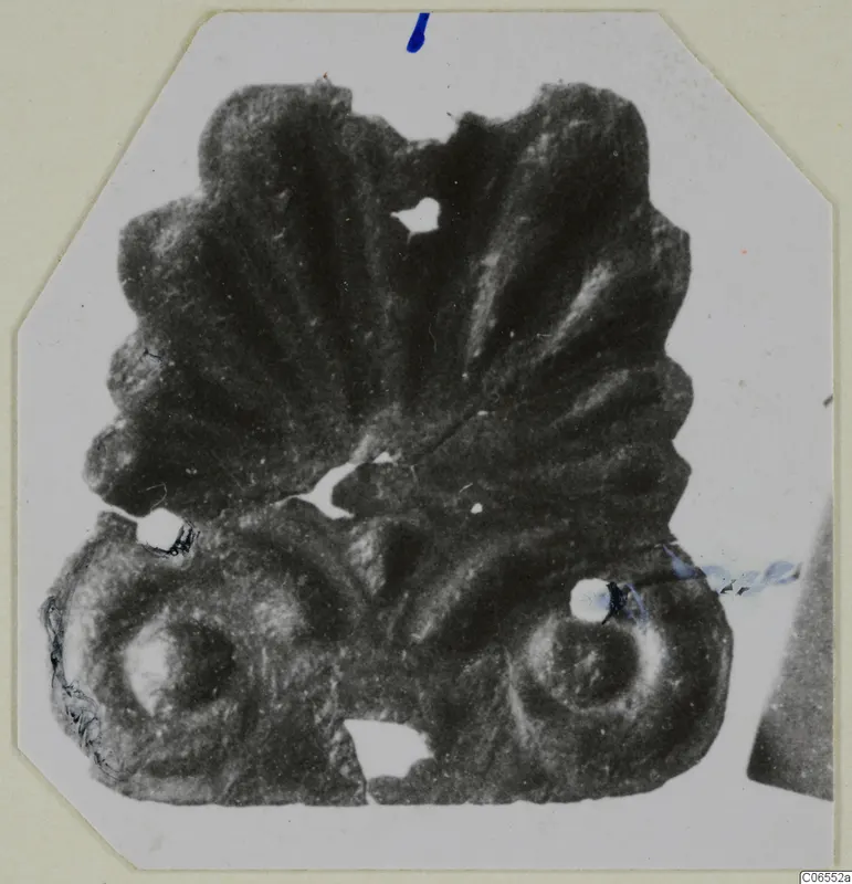 Bronze mounting fragment from Vouni with a fan-shaped top of radiating ridges and two round scrolls at the base.