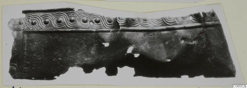 Fragment of a bronze sheet mounting with a row of bosses and wave-pattern relief along its upper edge