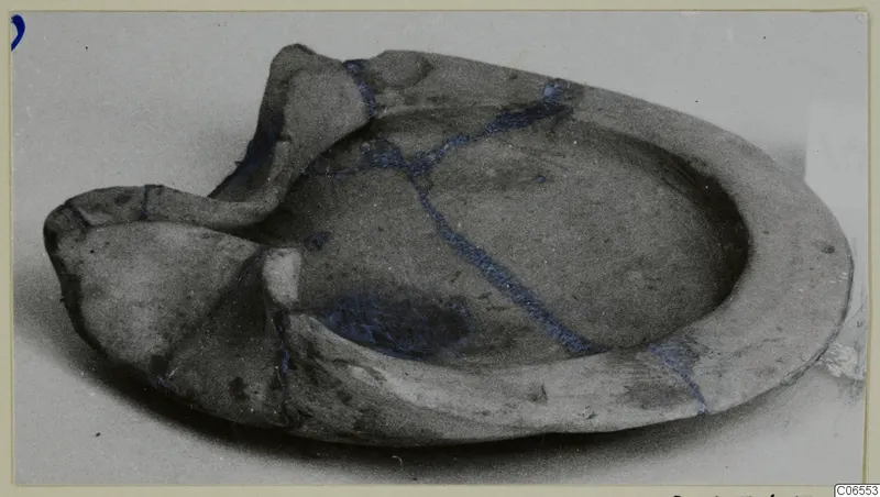 Terracotta lamp, broken and mended, with a raised spout and blue lines marking the joins