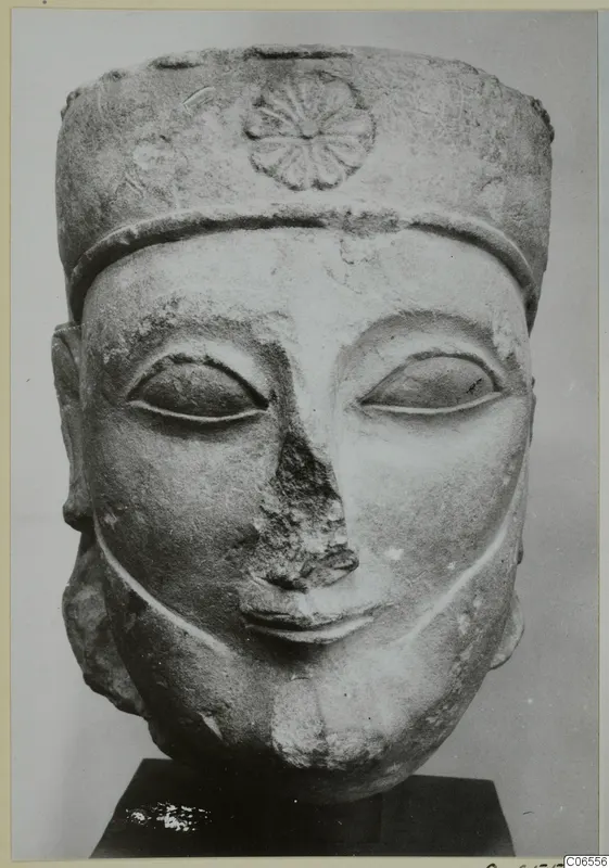 Limestone head sculpture with a tall cylindrical headdress decorated with a rosette, nose broken