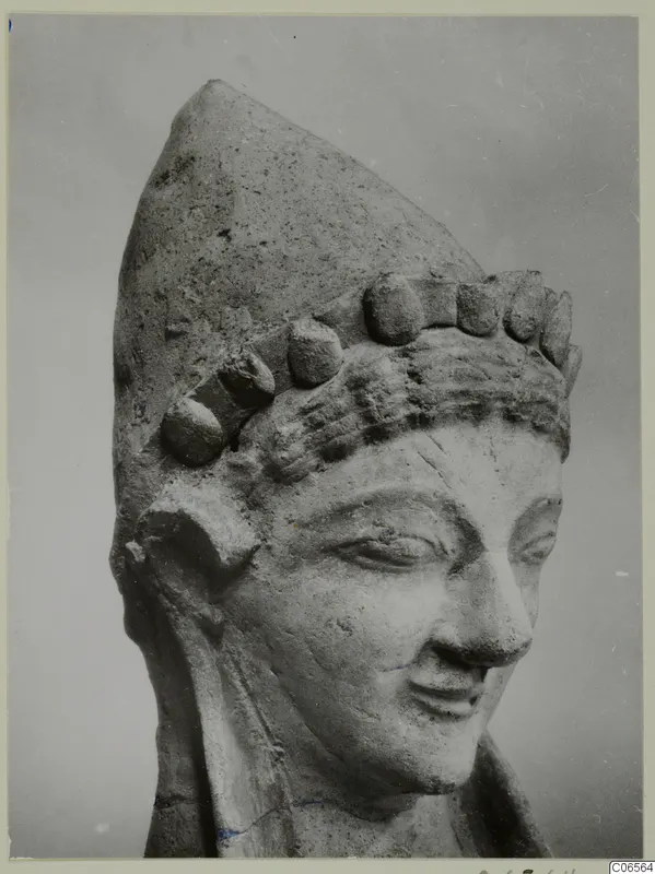 Terracotta head of a figure with a tall pointed headdress studded with knobs, from Mersinaki