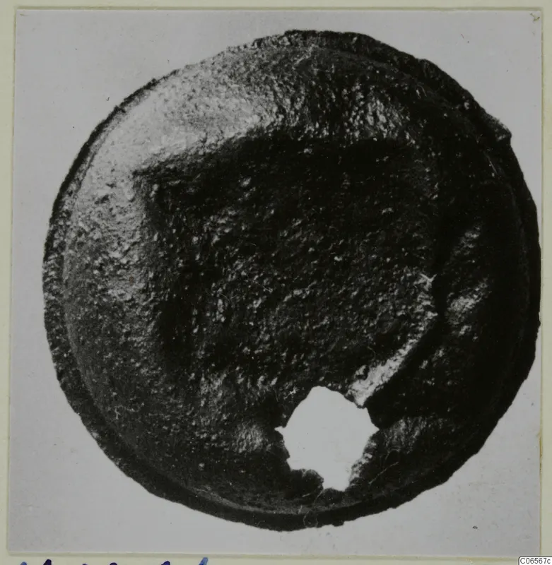 Round corroded bronze fragment with a broken hole at the lower edge, photographed from above on a mount.