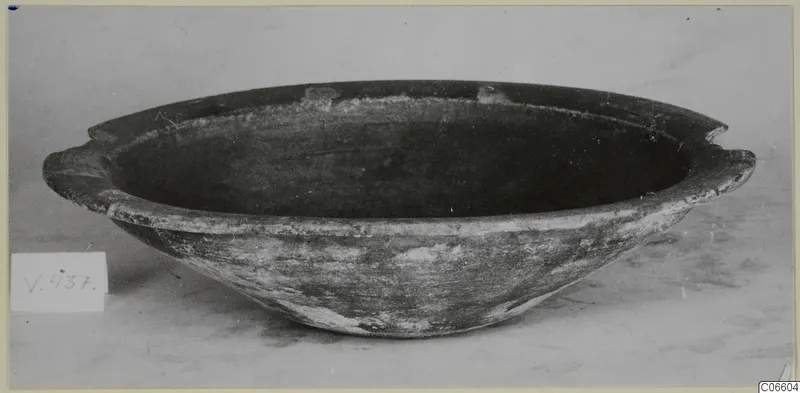 Pottery coarse ware bowl with two small horizontal handles and a dark interior, photographed as a find