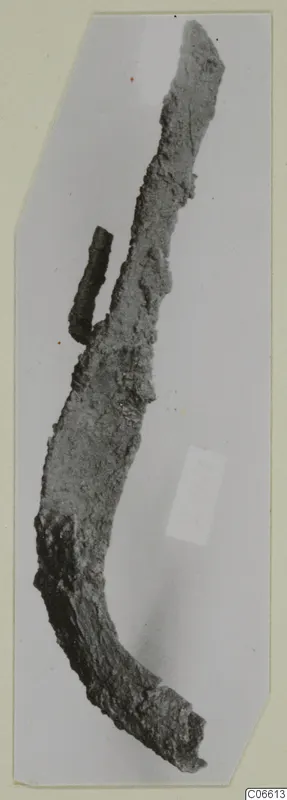 Corroded, curved iron tool from Vouni, with a short iron rod lying against its upper edge.