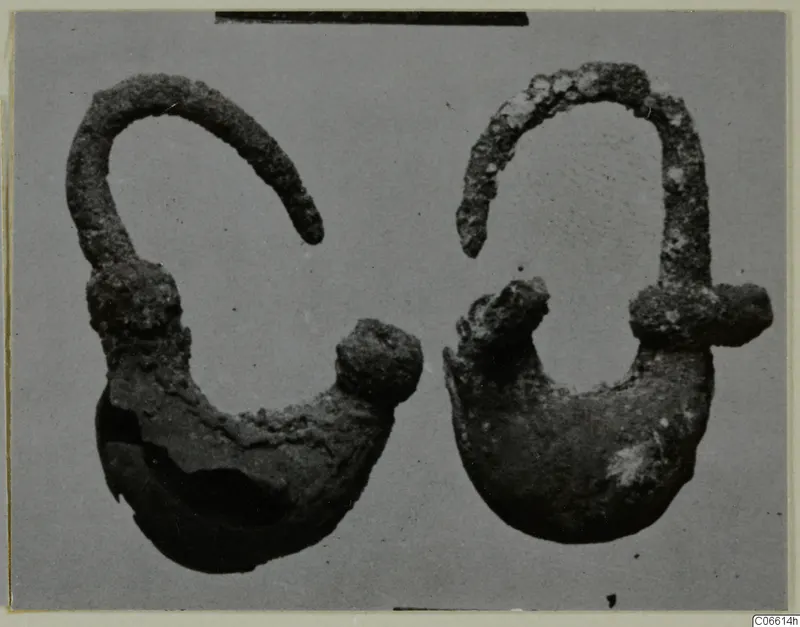 Two corroded metal ornaments, each with a curved wire loop and a rounded lower part with a knob