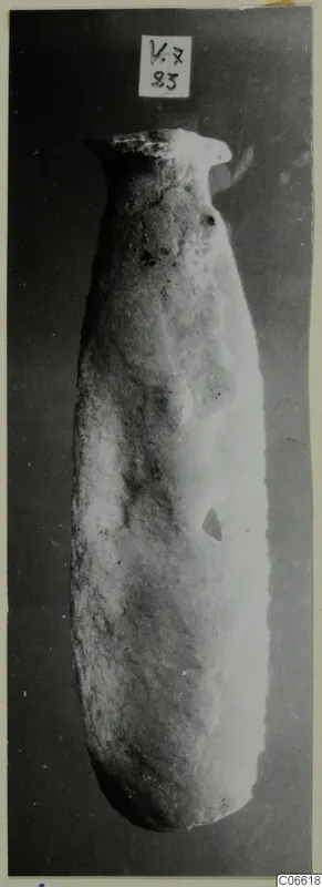 Tall pale stone vessel with a narrow flared neck, photographed against a dark background, from Vouni