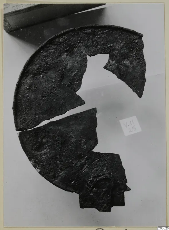 Broken fragments of a round bronze disc with a raised rim, on a pale background
