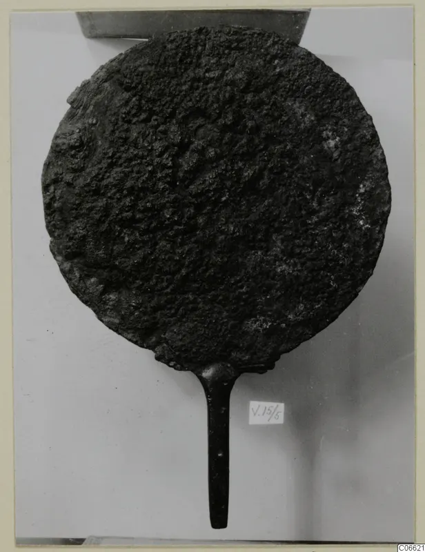 Bronze mirror with a long handle, its disc surface heavily corroded and pitted.