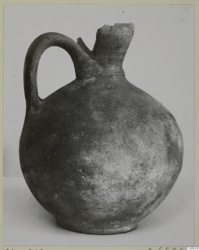Plain pottery jug with a single loop handle and a broken neck, shown against a light background.