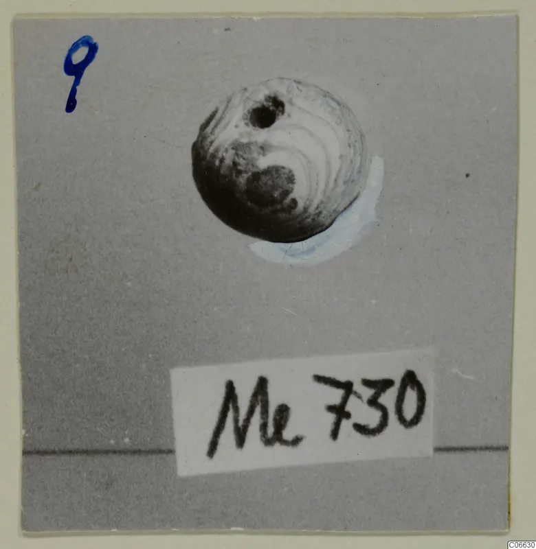 Round bead with a hole near the top, from Mersinaki, photographed on grey card.