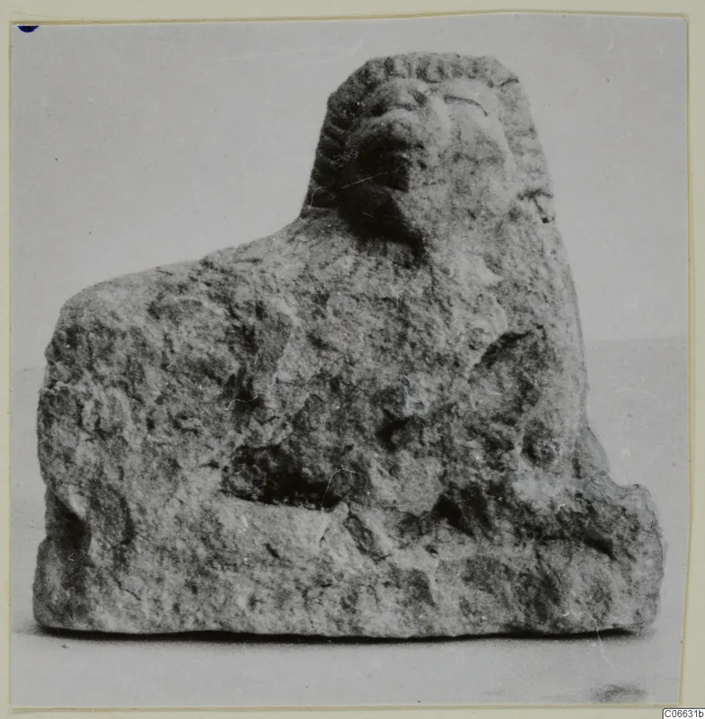 Small limestone figure of a crouching animal with a mane-like head, shown against a plain background.