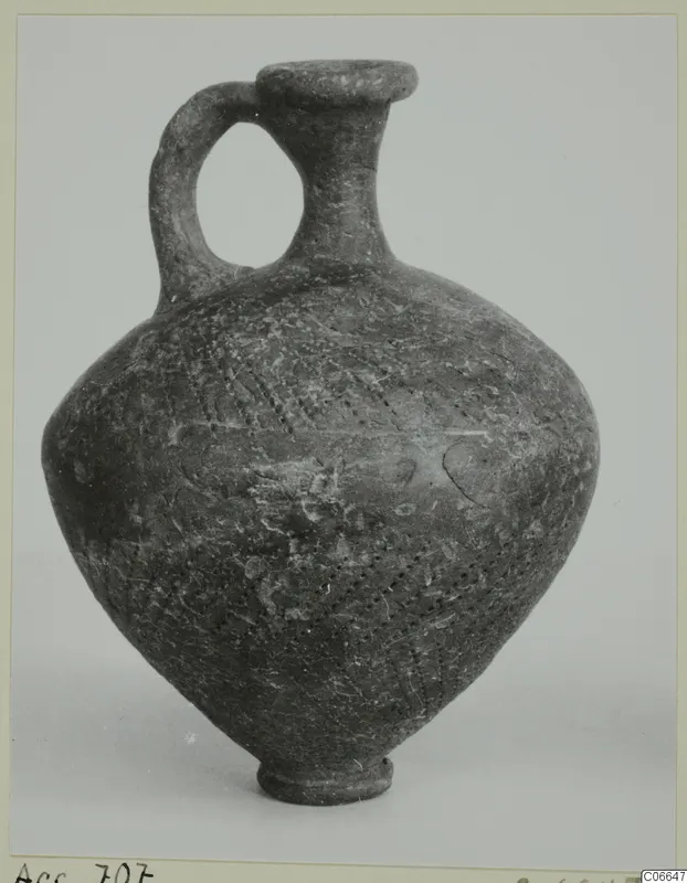 One-handled dark pottery jug with a narrow neck, flared rim and dotted decoration on the body.