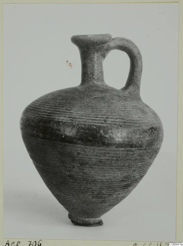 Black Lustrous Ware juglet with a single loop handle and horizontally ribbed body, shown against a grey backdrop