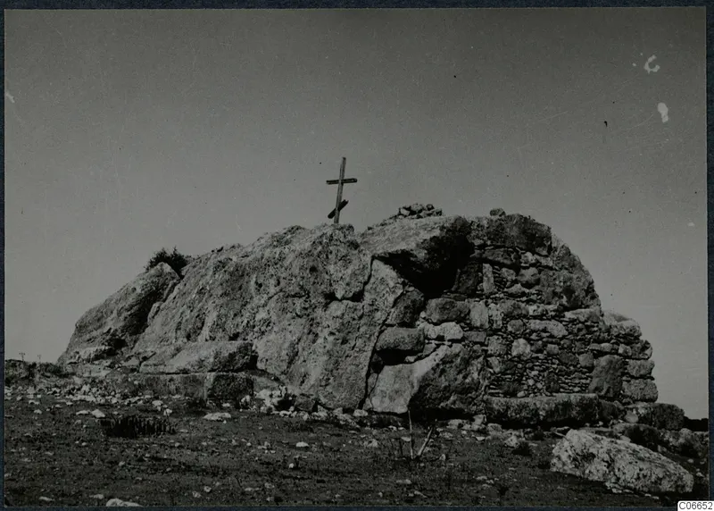 Built tomb of dressed stone with a wooden cross standing on top of a rocky mound