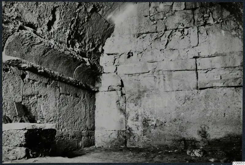 Interior of a built tomb chamber with large stone walls, a squared stone block and a small object at left