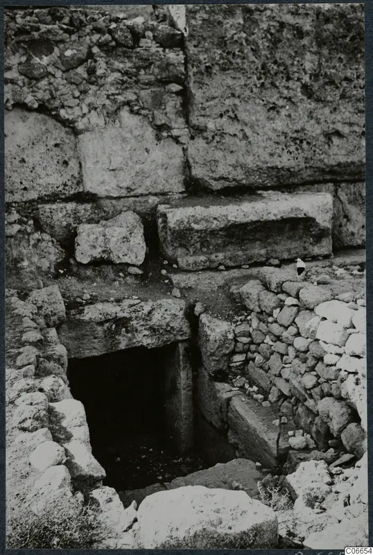 Built tomb with a dark doorway at the foot of stone steps, set among large masonry blocks and rubble walls