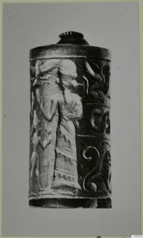 Cylindrical seal carved in relief with a standing figure in a long robe and spiral motifs, photographed on a grey card.