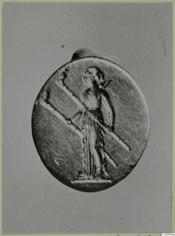 Oval gold pendant with a relief of a standing figure in profile holding a long diagonal staff