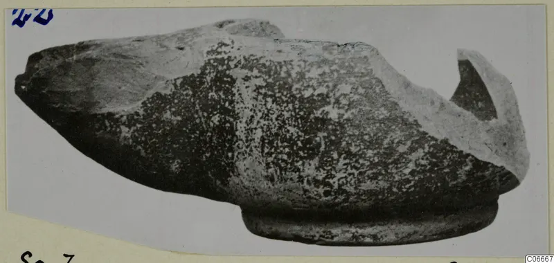 Terracotta oil lamp with a broken nozzle, shown in side view on a pale mount.
