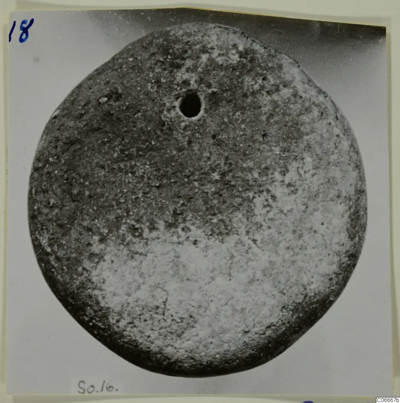 Round disc-shaped find with a small hole near its upper centre, photographed on a mounted card, from Soli