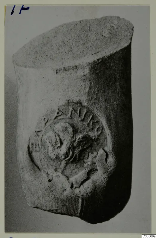 Cylindrical object with a raised circular medallion showing a head in profile and partly legible letters around its rim