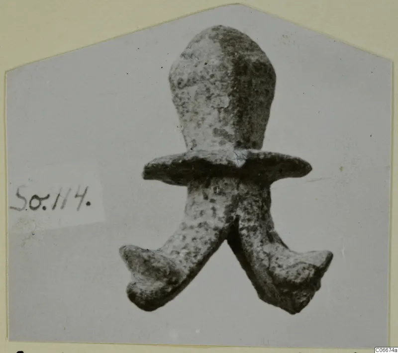 Corroded metal object with a rounded upper part, a flat flange across the middle and two splayed prongs below