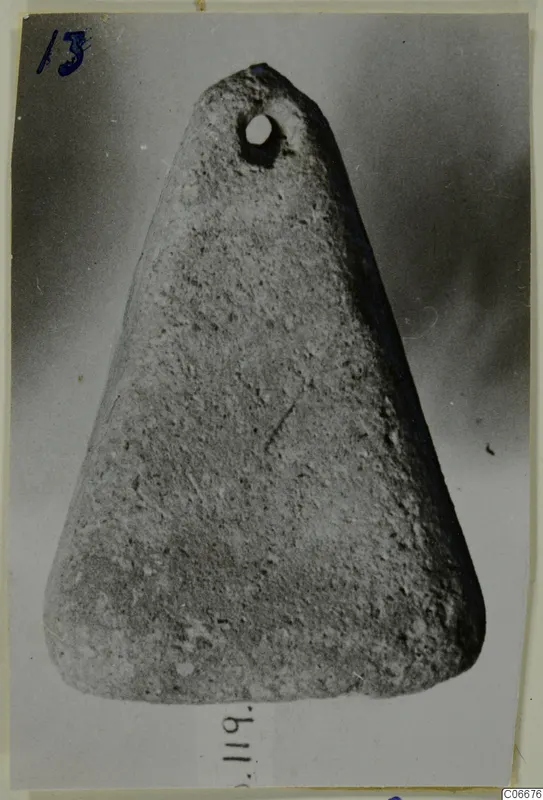Triangular object with a round perforation near its narrow end, photographed against a dark grey backdrop