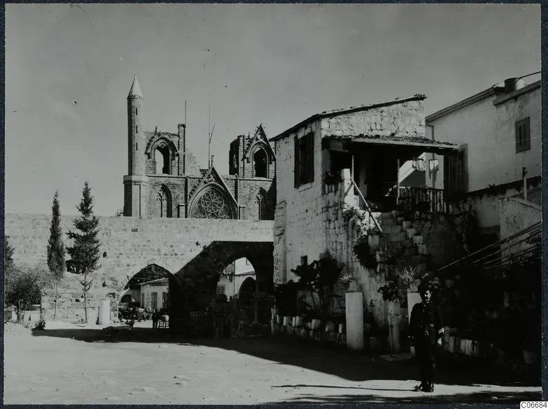 Church ruin with a tall pointed tower behind an arched stone wall at Famagusta, with a man standing in the street