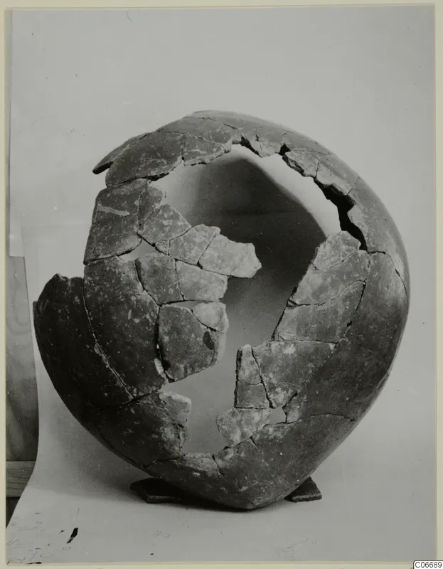 Broken pottery jug from Lapithos, partly reassembled from fragments, standing on a small wooden stand.