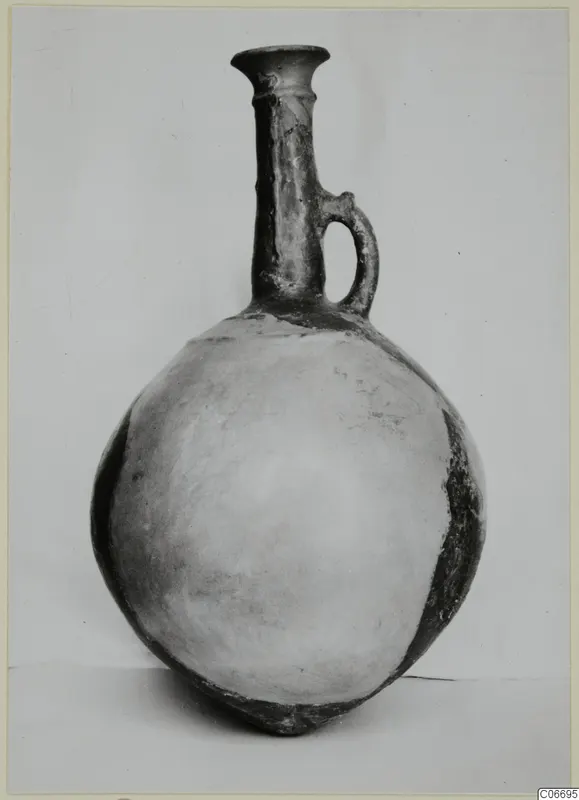 Pottery jug with a tall flared neck and single loop handle, photographed against a plain backdrop
