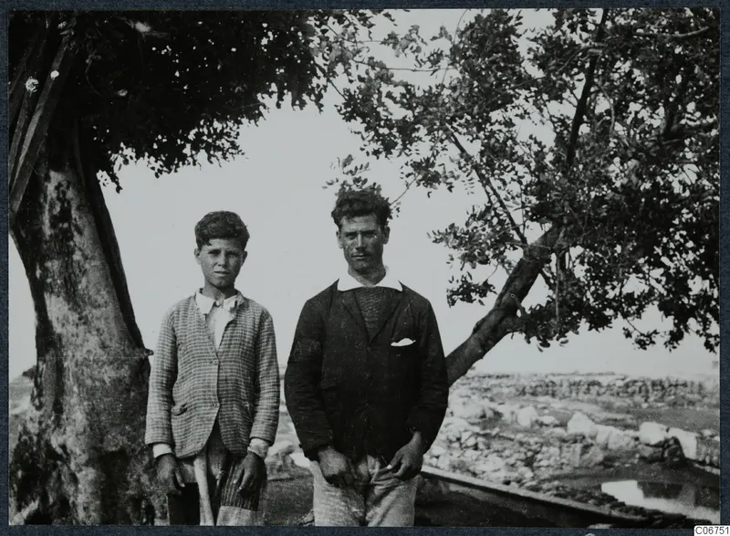 Two people standing beside a large tree at Vouni, with a stony field behind them
