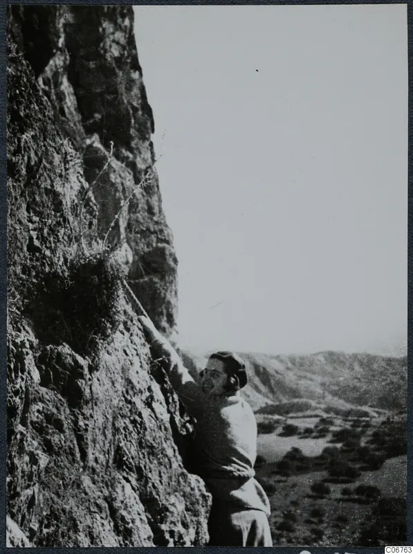 Joan du Plat Taylor climbing a rock face at Fylleri, with a valley and hills stretching behind her.
