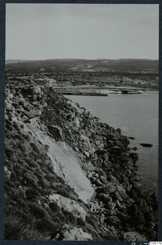 Rocky coastline with a steep cliff falling to the sea, with low hills behind