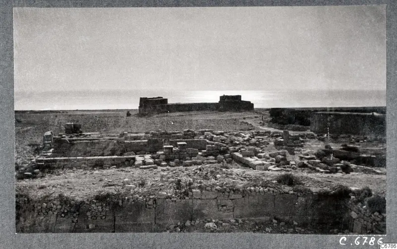 Ruins of the Temple of Aphrodite at Kouklia: low stone walls and scattered blocks, with a ruined building and the sea beyond