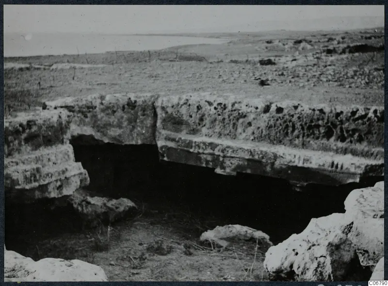 Pale weathered stone slabs over a dark recess, with flat land and sea behind