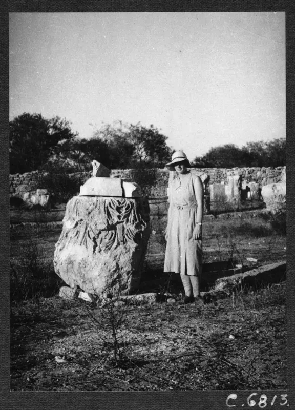 Woman in a light dress and wide-brimmed hat standing beside a carved stone block with broken fragments on top, at Salamis