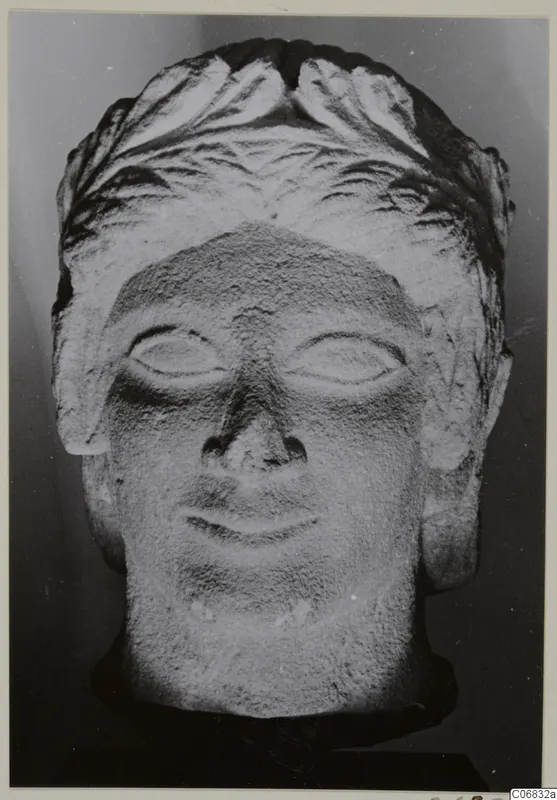 Limestone head of a figure with carved wavy hair and a slight smile, seen from the front