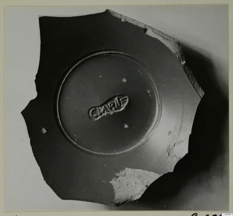 Pottery sherd with a raised central ring and a stamped oval impression, photographed on a light background