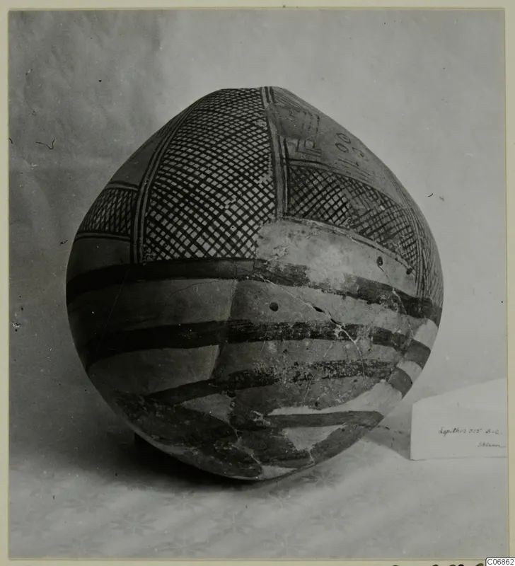 Round-bodied painted pottery vessel with cross-hatched panels and dark bands, photographed on a cloth backdrop.