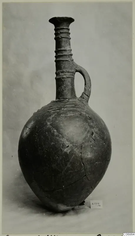 Pottery jug with a tall ringed neck, single loop handle and rounded body, photographed against a plain grey background.