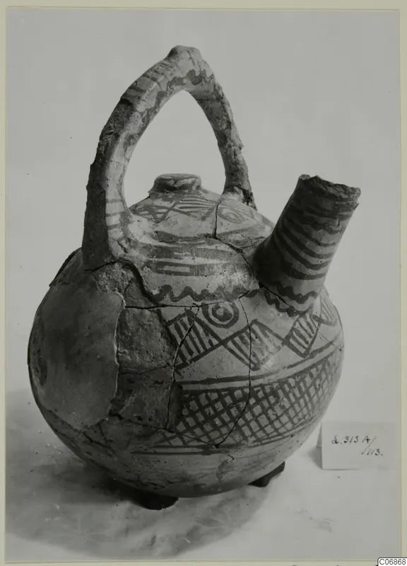 Jug with a strap handle, a side spout and painted geometric bands in dark paint on a pale ground