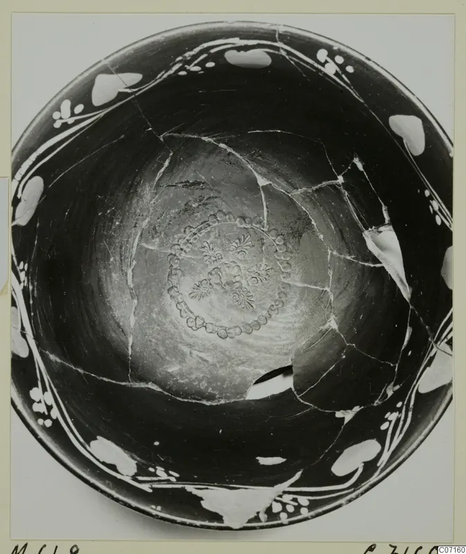 Interior of a broken dark bowl with white painted rim decoration and a stamped rosette at the centre