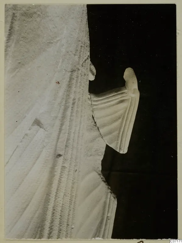 Close view of a white limestone sculpture fragment from Vouni, with carved parallel folds, photographed against black.