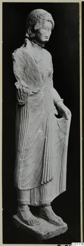 Limestone statue of a standing woman with a curled headdress, from Vouni, shown against a black background