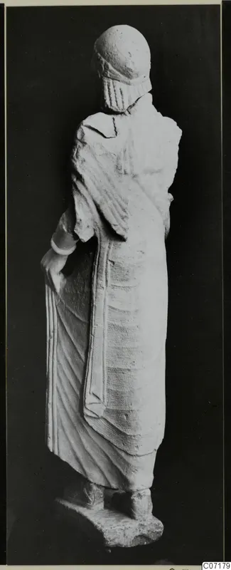 Back view of a limestone statue of a standing woman from Vouni, against a dark background