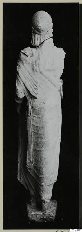 Back view of a standing limestone statue from Vouni, wearing a cylindrical headdress and long draped garment.
